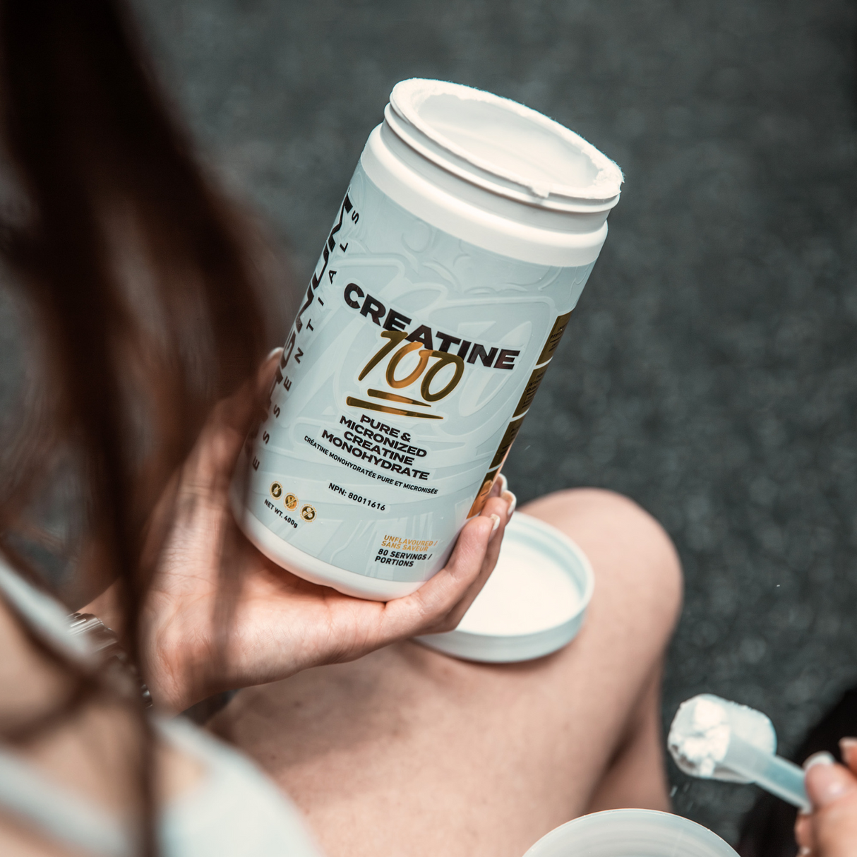 A person holding an open container of Magnum Nutraceuticals Creatine 100, ready to scoop the unflavored micronized creatine powder for mixing.