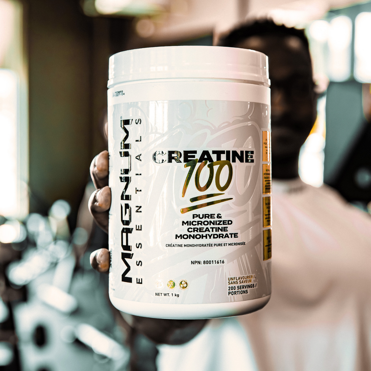 A close-up of a hand holding a container of Magnum Nutraceuticals Creatine 100, prominently displaying the label with the product's key features in a gym setting.