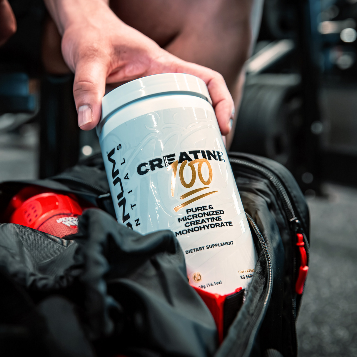 A person placing a container of Magnum Nutraceuticals Creatine 100 into a gym bag.